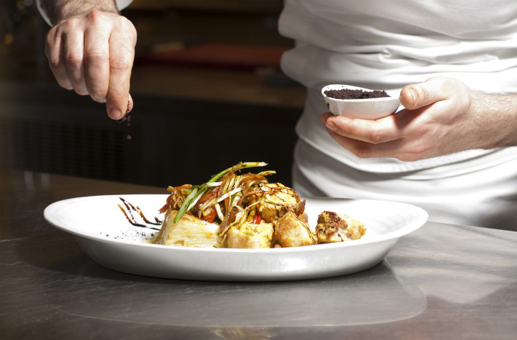 Chef seasoning a dish with a brown powder