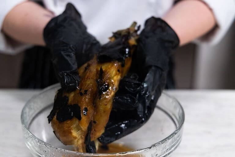 Chef wearing black gloves prepares a babaganoush