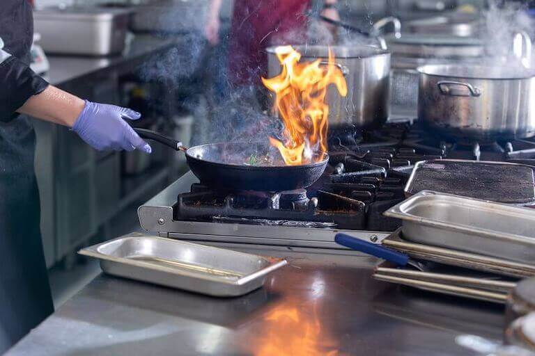 Chef cooking in commercial kitchen with flames coming out of a pan