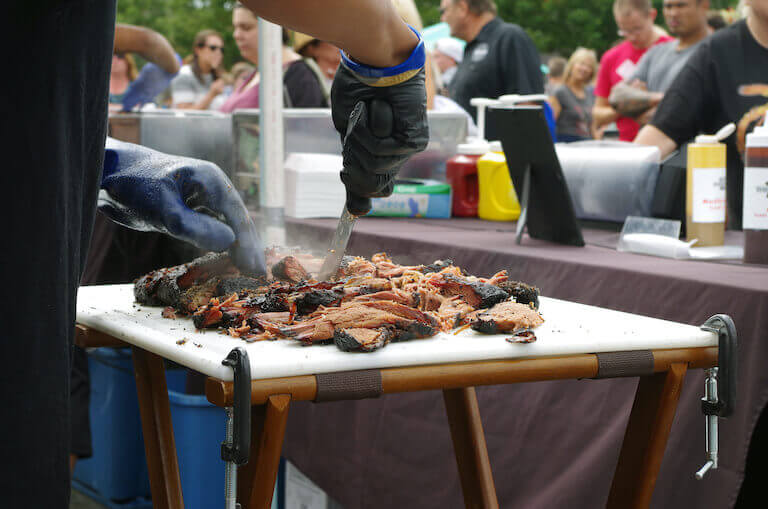 Chef slicing beef on a white cutting board at an outdoor food event