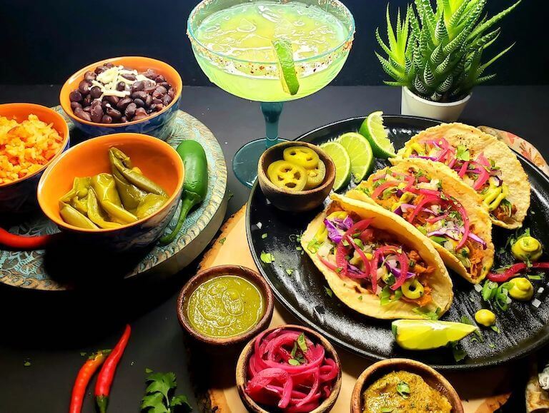 Jackfruit tacos displayed on a table with with rice, sauces, and a drink