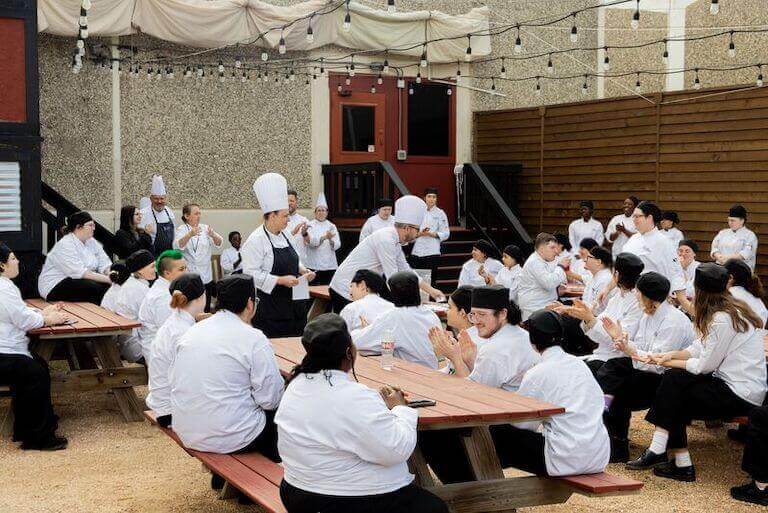 Large group of Escoffier students sitting outside at picnic tables talking to each other