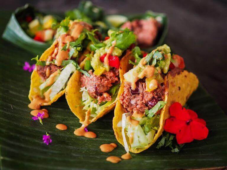 Three jackfruit vegan tacos topped with lettuce and sauce on a green plate