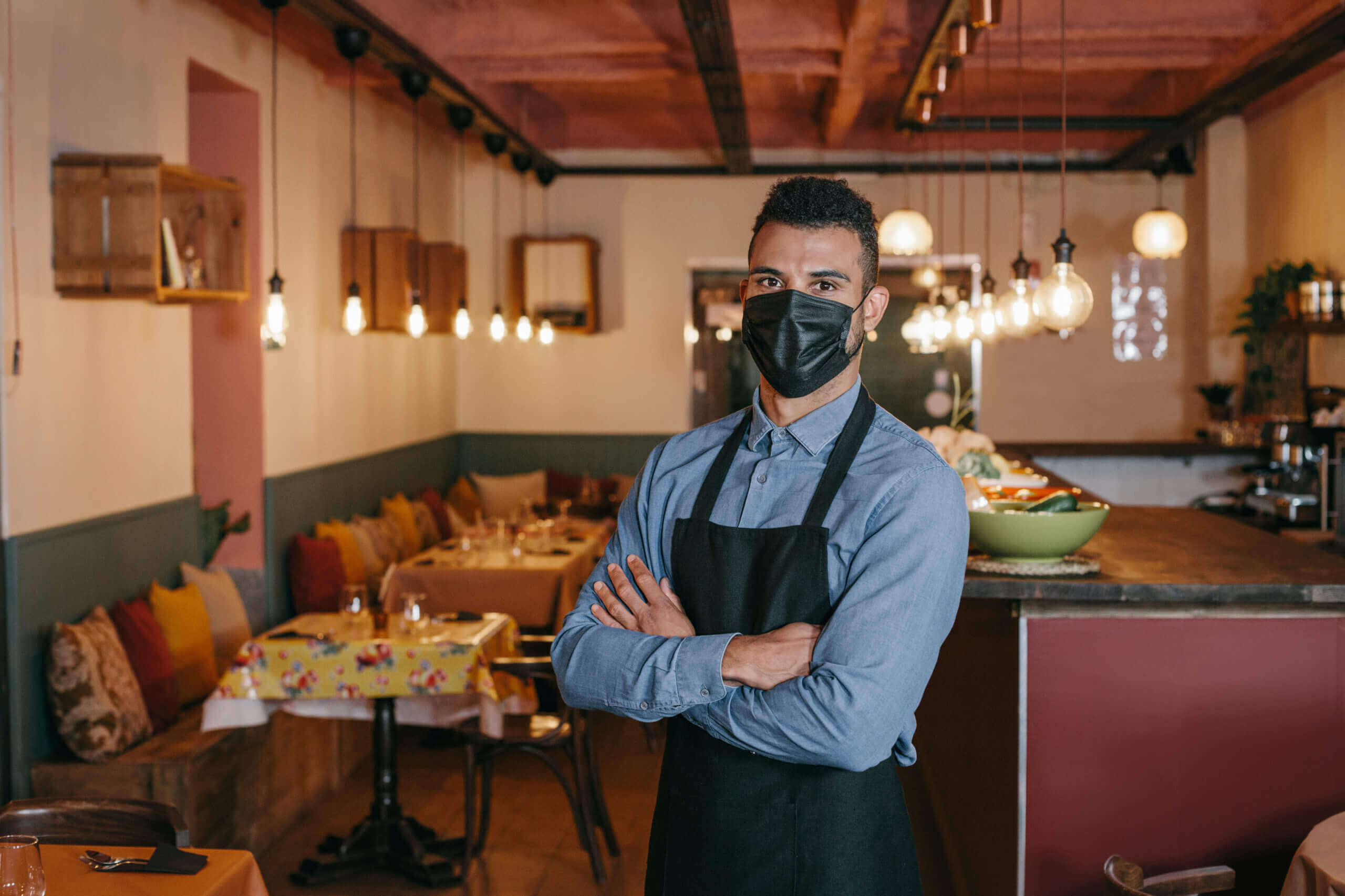Businessman wearing a protective black face mask and standing at his restaurant during Coronavirus