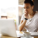 Female student taking notes while looking at computer with earphones