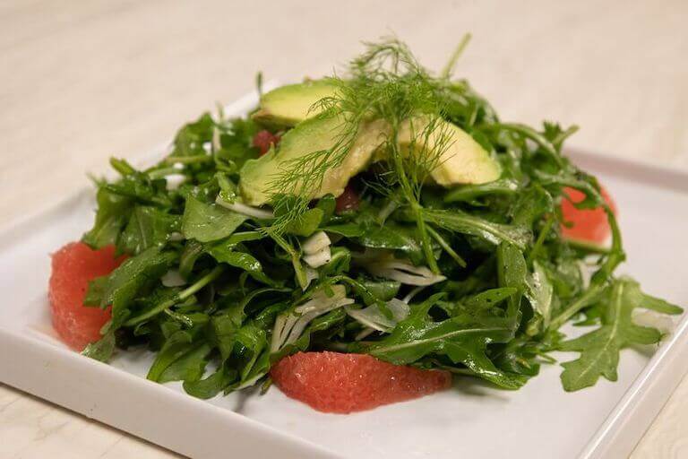 Fennel salad topped with avocado on a square white plate