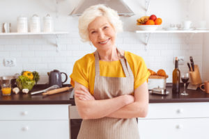 Happy older woman in apron preparing breakfast, crossed hands