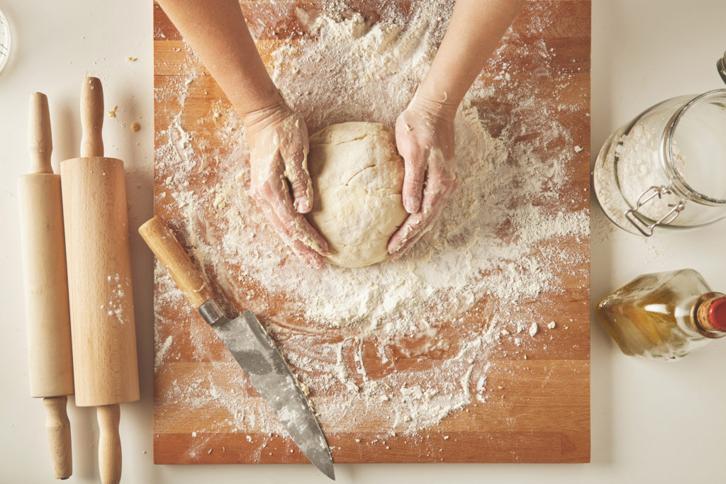 Kneading dough on wooden board with rolling pins and knife and flour