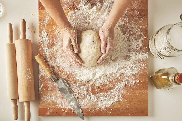 Kneading dough on wooden board with rolling pins and knife and flour