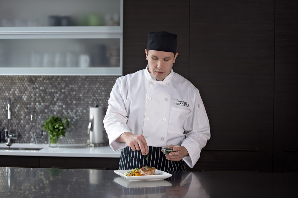 Male culinary student garnishing a vegetable and meat dish in home kitchen