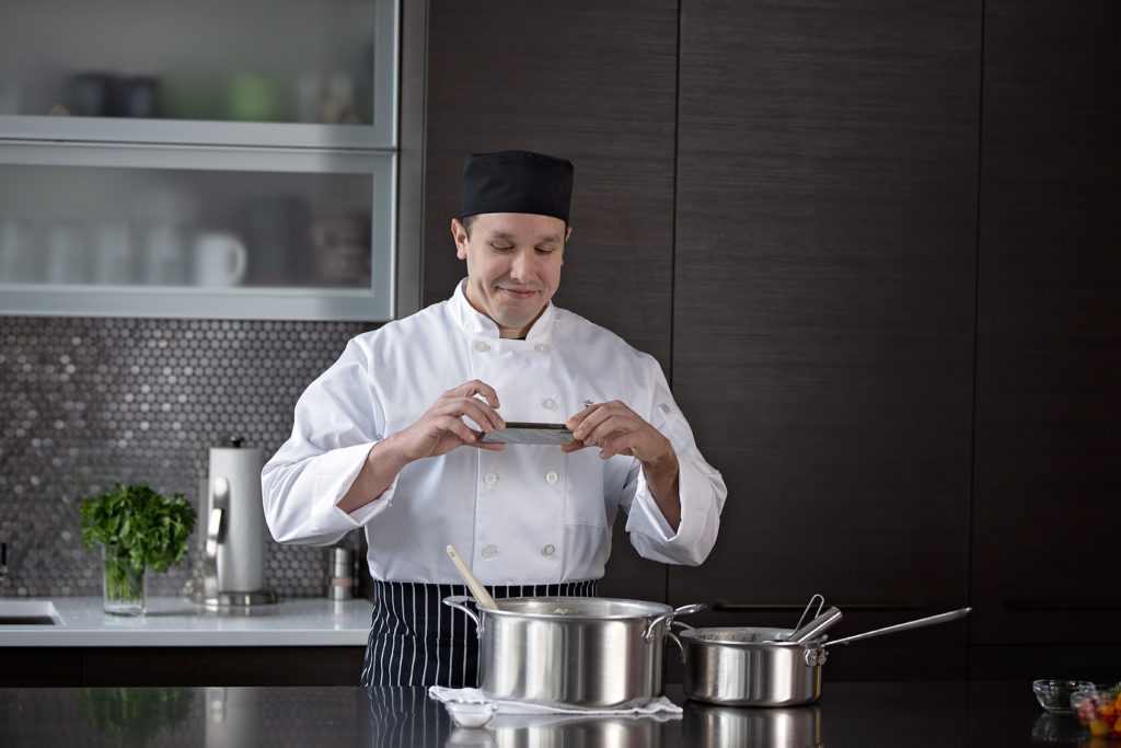 Smiling male chef taking photo of metal pot on his phone