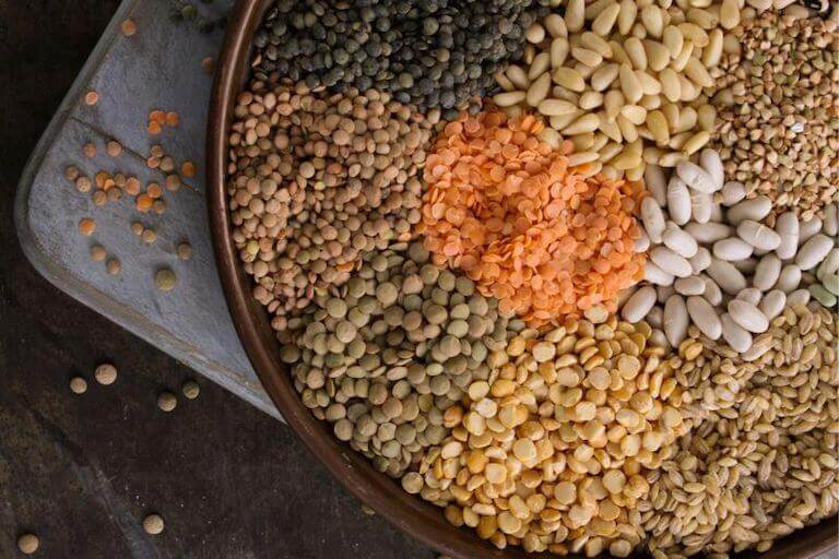A basket showing several types of lentils, white beans, buckwheat, and barley grains.