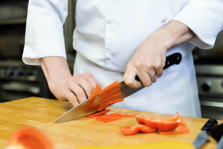 Chef slicing red bell peppers on a wooden cutting board
