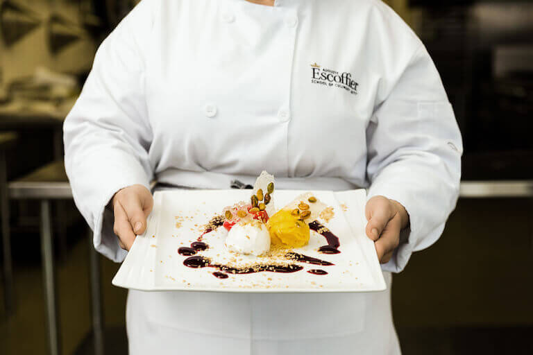 Escoffier student in uniform holding a plated dessert with ice cream