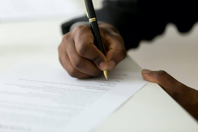 Person signing paper document with a black and gold pen