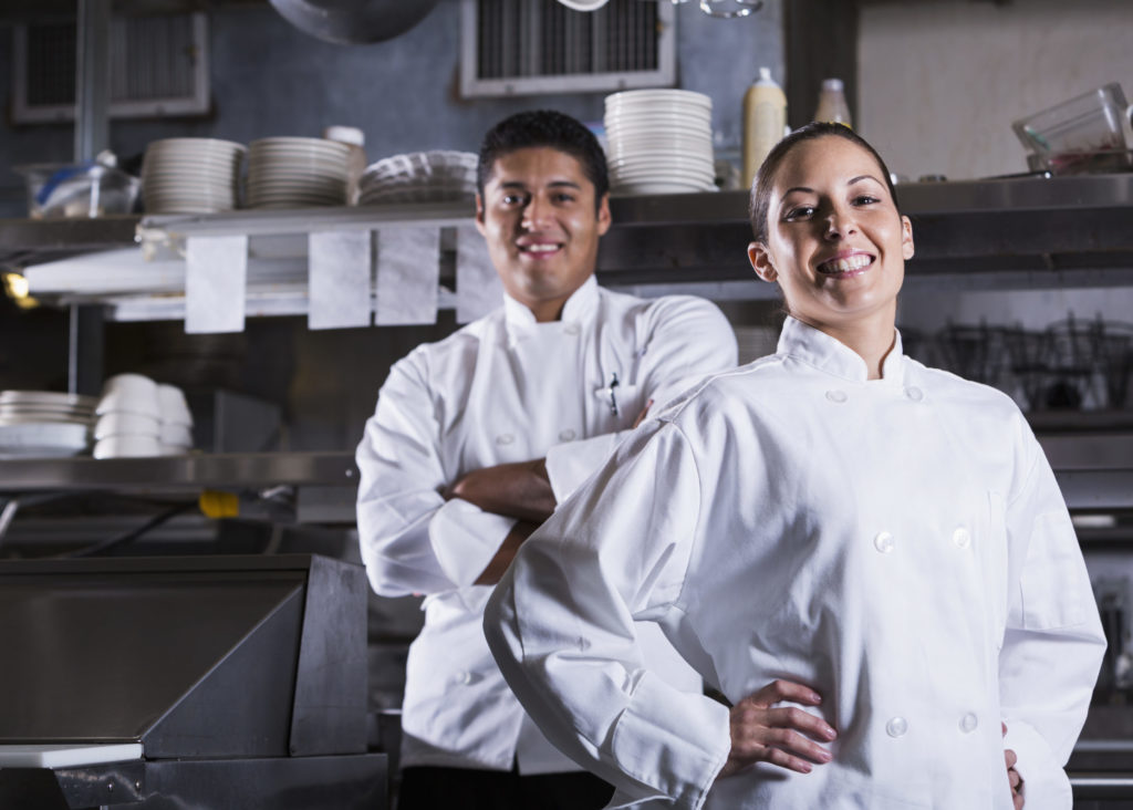 Smiling male and female cooks in commercial kitchen