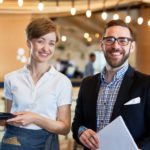 Cheerful bearded restaurant manager and pretty waitress posing for photography while standing against bar counter