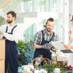 Event planner using checklist while examining delivery of crockery and decorations while positive movers unpacking boxes