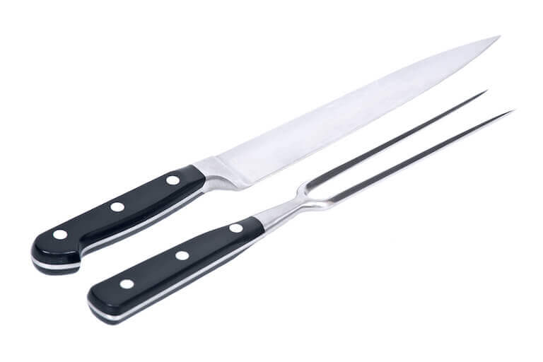 A closeup of a carving knife and a carving fork set against a plain white background