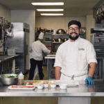 smiling male culinary student with bear din commercial kitchen with bacon peanuts ham