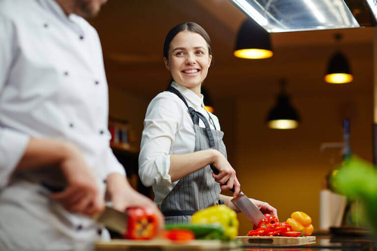 Two smiling chefs cutting red and yellow bell peppers with a knife