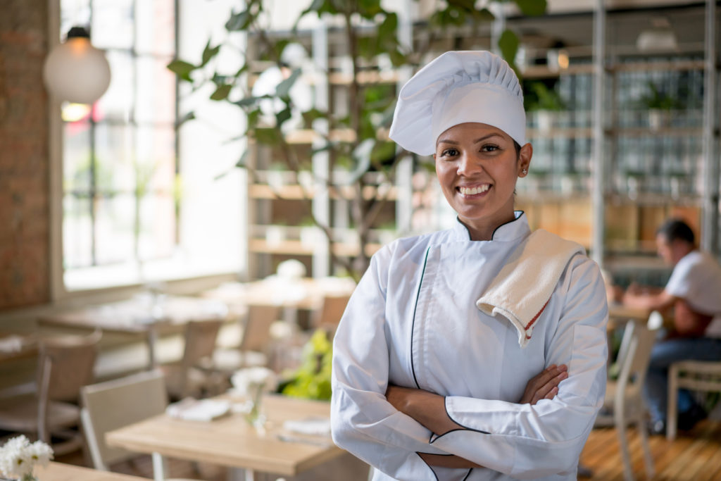 Smiling female chef in restaurant with towel and white chef hat