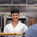 Smiling female chef with black hat holding baked french bread baguette