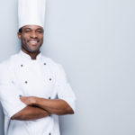 Smiling male black chef with white coat and hat
