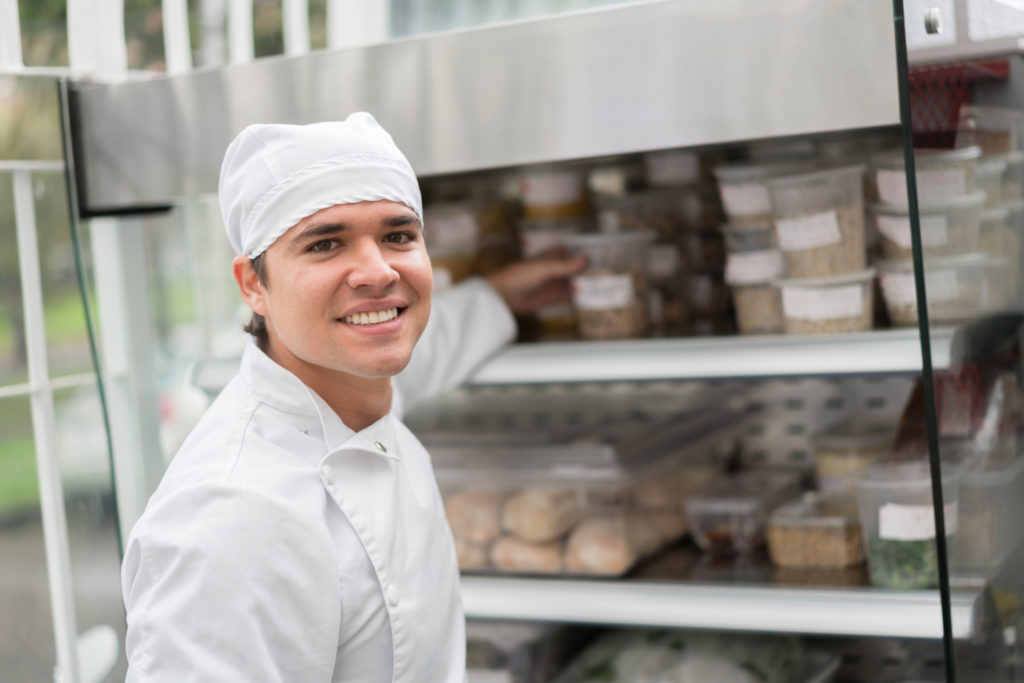 Smiling male cook with white hat holding plastic jar container
