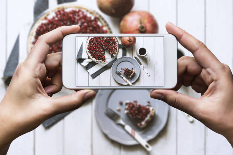 A pair of hands holds a white cell phone over a festive pie with an image of the pie displayed on the phone’s screen.