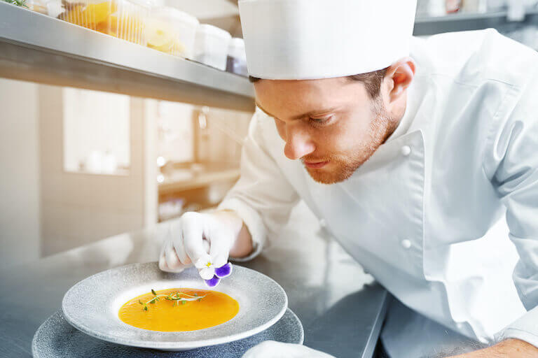 male chef decorating plate of soup with flower in a restaurant kitchen