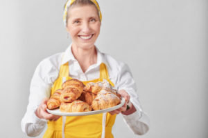 Chef Colette Christian in a yellow apron holding plate of croissants