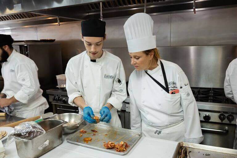 Chef instructor watching a student make skewers in a kitchen
