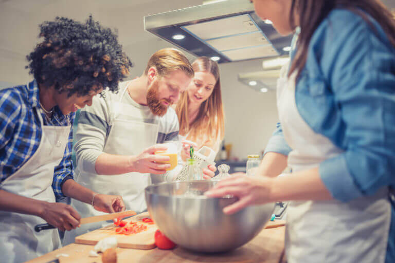 Cook with beard holding cheese grater with three other cooks