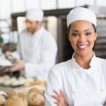 Smiling female chef in a bakery with loaves of bread