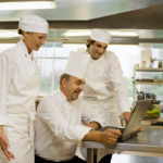Three chefs looking at a laptop
