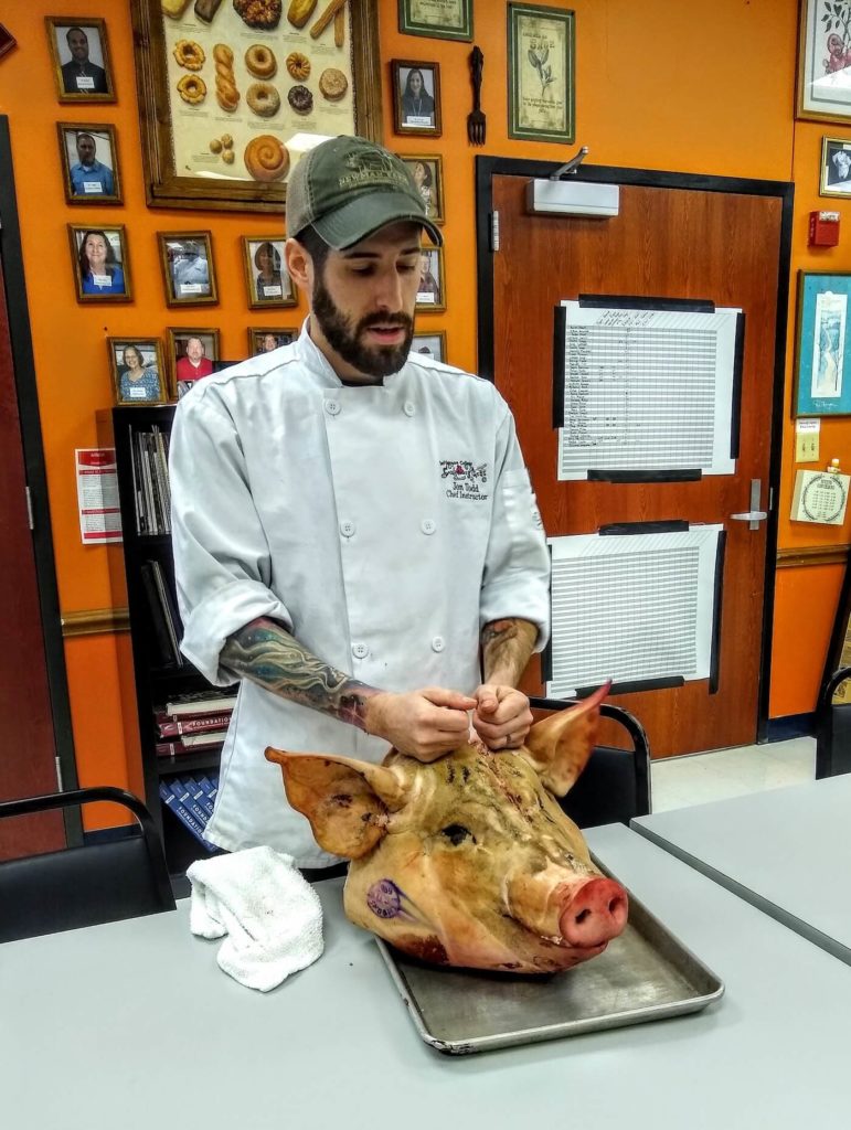 Chef Jon teaching position giving a lecture on whole animal butchery with a pigs head.jpg