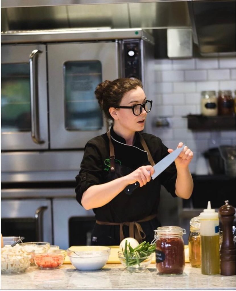 Escoffier Chef Instructor Stephanie Michalak White holding a knife while doing a cooking demo