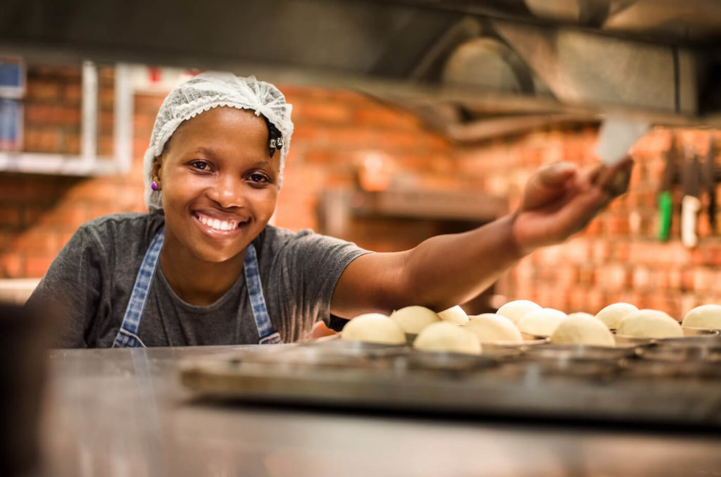 Smiling black female chef with apron and baking tray with dough