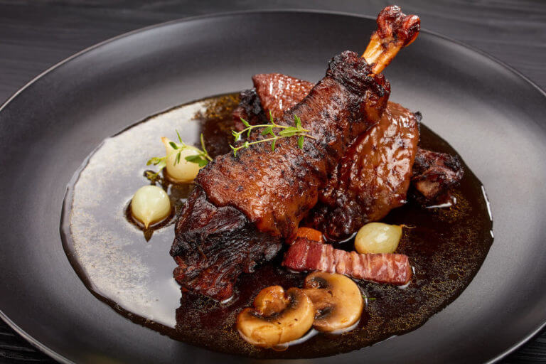 close-up of a portion of Coq Au Vin, chicken mushrooms on black plate