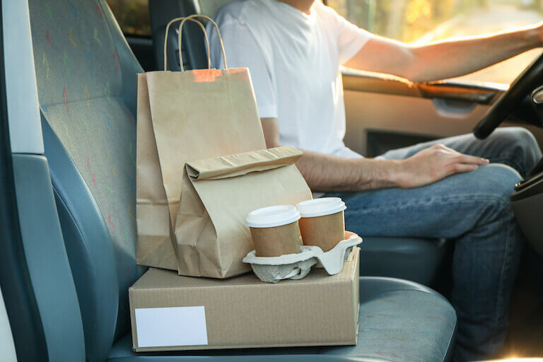 Brown paper to go bags and coffee sitting on the seat of a car