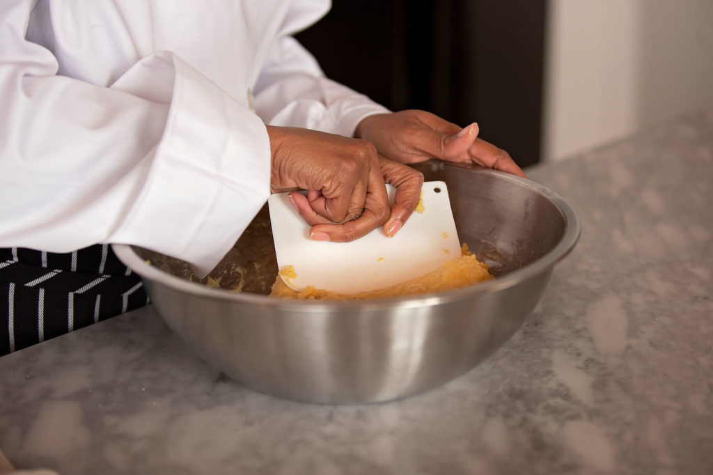 Escoffier online student kneading dough in a metal bowl with scraper