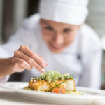 Female chef plating and garnishing a breaded chicken dish