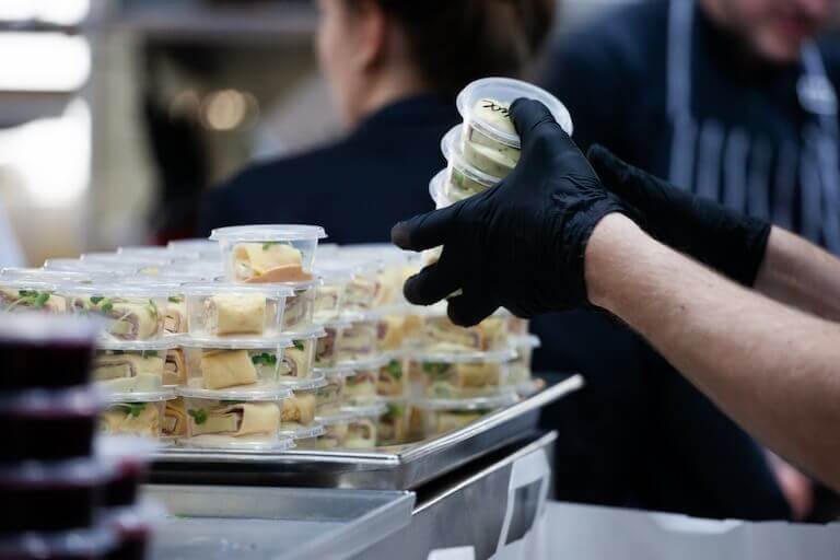 Restaurant employee wearing black gloves picking up clear to go containers filled with food