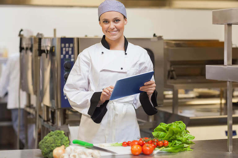 Smiling chef holding tablet in kitchen in front of vegetables