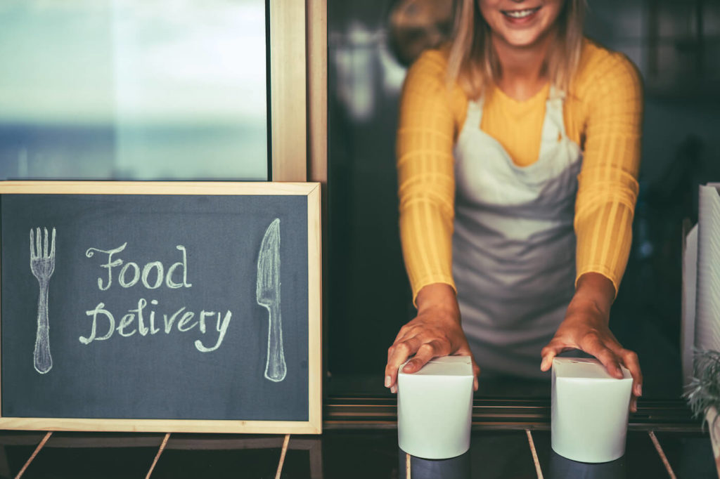 Young woman with apron serving healthy takeaway with food delivery sign