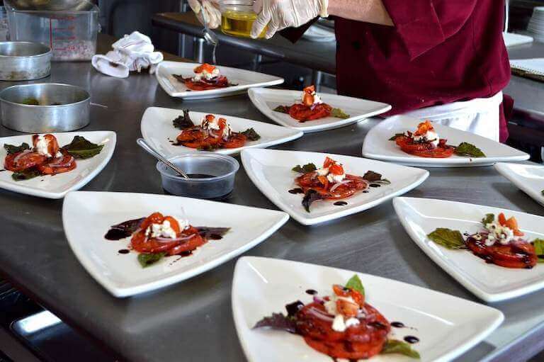 Chef plating white dishes with tomatoes and feta cheese