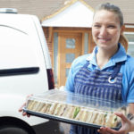 Smiling Female Caterer Delivering Tray Of Sandwiches To House