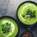 Green plant based soup in a black bowl with broccoli and peas