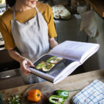 Happy woman with apron reading a cookbook in the kitchen 